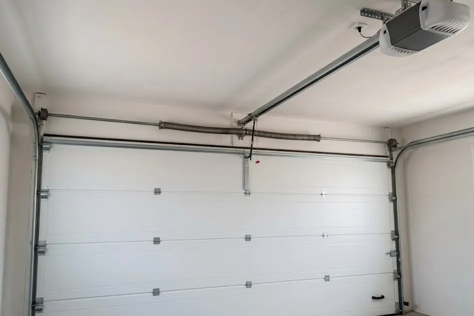 Inside a garage showing the torsion spring above a sectional door, the tracks and a ceiling-mounted opener