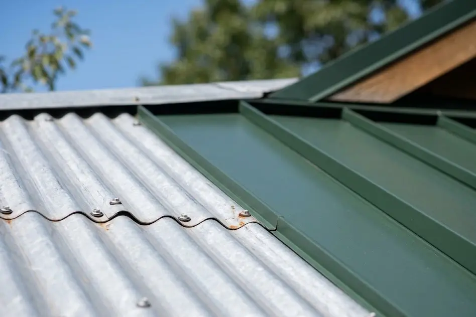Close-up of corrugated metal roof panels with exposed screws next to green standing seam panels with raised seams