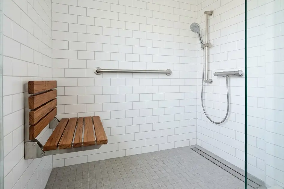 Walk-in shower with a stainless steel grab bar, a fold-down bench and a handheld shower head on a slide bar